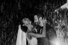 a bride and groom are standing in the rain with their arms around each other as they laugh