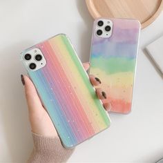 two phone cases with rainbow paint on them, one being held by a woman's hand