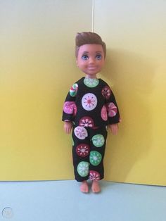 a doll is standing next to a yellow wall wearing a black pajamasuit with colorful buttons on it