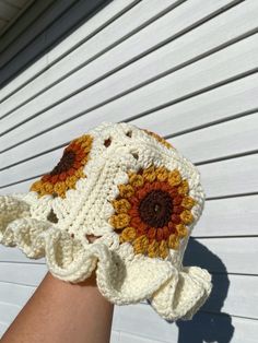 a crocheted sunflower hat on someone's hand with white siding in the background