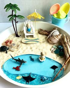 a bowl filled with toys and sand on top of a white table next to a palm tree