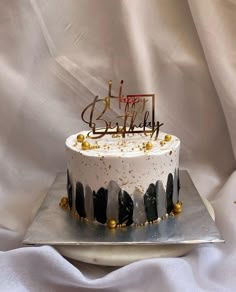 a white and black birthday cake on a silver platter with gold sprinkles