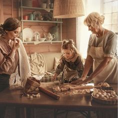 three women standing around a wooden table with food on it and one woman looking at something in the distance