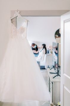 a wedding dress hanging on a hanger in a bridal room with people sitting at tables