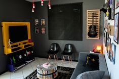 a living room with grey walls and black chairs, yellow entertainment center, and pictures on the wall