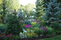 a garden filled with lots of different types of flowers and plants next to some trees