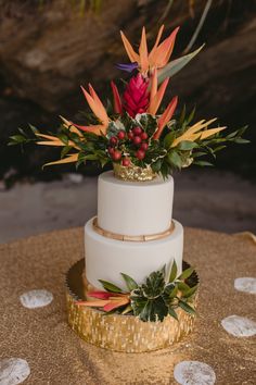 a three tiered wedding cake decorated with flowers and greenery on a gold tablecloth