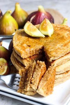 a stack of pancakes sitting on top of a white plate next to some figs