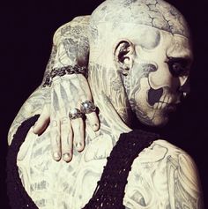 a man with tattoos and piercings on his chest wearing a black tank top in front of a dark background