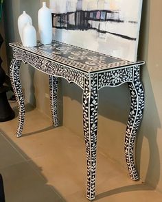 a black and white table with two vases on it next to a large painting