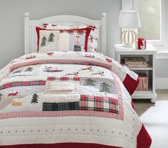 a white bed topped with a red and green quilted comforter next to a night stand