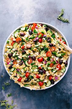 a large bowl filled with pasta salad on top of a blue countertop next to a wooden spoon