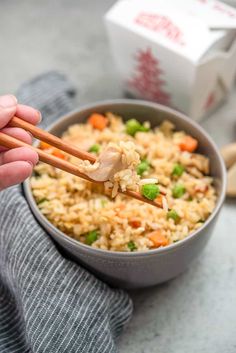 someone holding chopsticks over a bowl of rice with peas and carrots in it