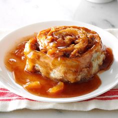 a white plate topped with an apple cinnamon roll covered in caramel sauce next to a cup of coffee