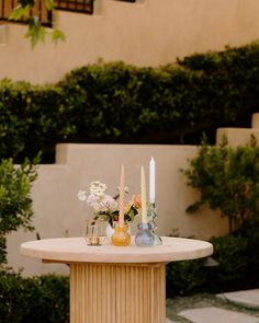 a table with candles and vases on it in front of some bushes, shrubs