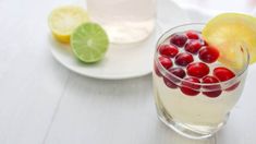 a drink with cranberries and lemon wedges on a white table next to another beverage