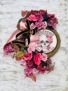 a wreath with flowers and a skull on it sitting on a white wooden surface next to a ribbon