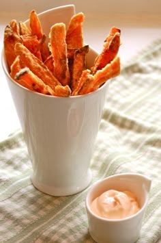 a white cup filled with sweet potato fries next to a small bowl of ranch dip