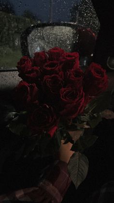 a bouquet of red roses sitting in the back seat of a car on a rainy night