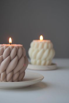 two candles sitting on top of a white plate next to each other in front of one another