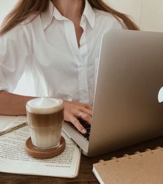 a woman sitting in front of a laptop computer with a cup of coffee next to her