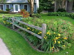 a wooden fence in front of a house with flowers growing on the lawn and around it