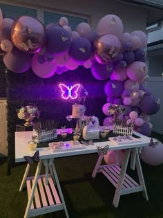 a white table topped with lots of purple and white balloons next to a wall covered in butterflies