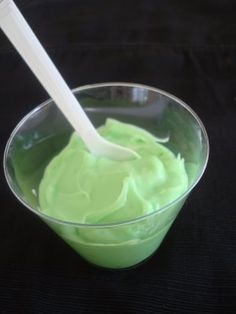 a plastic cup filled with green liquid and a white spoon in the bowl on a black surface