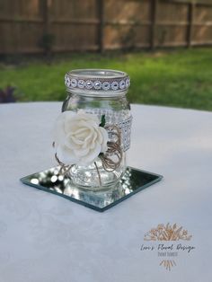 a glass jar with a white rose in it sitting on top of a metal tray