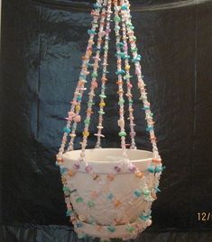 a white vase with multi colored beads hanging from it's side on a black background