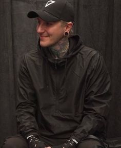 a man with tattoos sitting on top of a black chair wearing leggings and a baseball cap