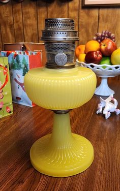 a yellow candle holder sitting on top of a wooden table next to a bowl of fruit