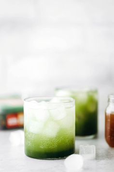 two glasses filled with green liquid and ice cubes next to each other on a table