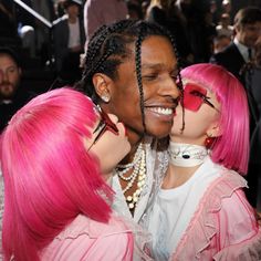 two women with pink hair are kissing each other at the same time as people look on