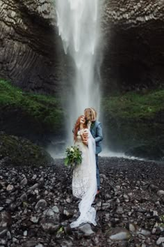 a bride and groom standing in front of a waterfall