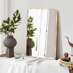 a mirror sitting on top of a wooden table next to a vase filled with plants