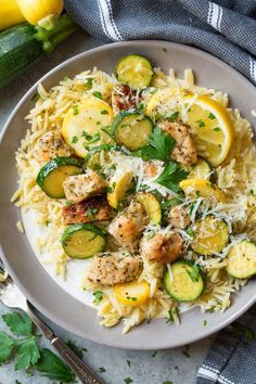 a plate of pasta with zucchini, chicken and parmesan cheese on top