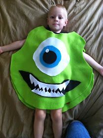 a little boy laying on top of a bed wearing a green monster costume with big eyes