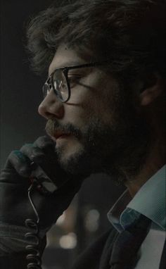 a man with glasses is talking on a cell phone in the dark, wearing a suit and tie