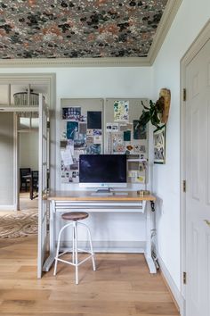 a desk with a computer on top of it in front of a wall full of pictures