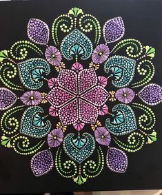 an intricately designed painting on black paper with purple, green and blue flowers in the center