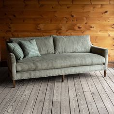 a green couch sitting on top of a wooden floor next to a wood paneled wall