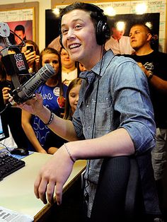 a man with headphones on is in front of a laptop and microphone while people look at him