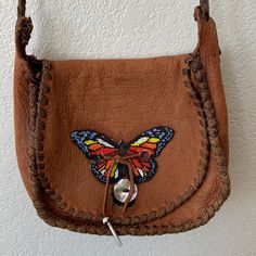 a brown leather purse with a butterfly on the front and side flap, hanging from a hook