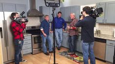 three men in a kitchen talking to one another while the camera man is filming them