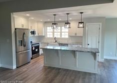 an empty kitchen with stainless steel appliances and wood flooring, along with white cabinets