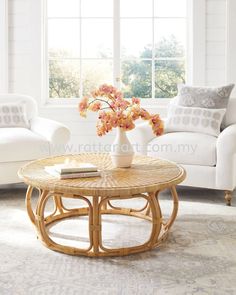 a wicker coffee table with flowers in a vase on top and two white couches behind it