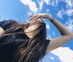 a woman with her hair blowing in the wind, looking up into the blue sky