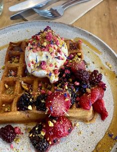 a waffle with fruit and whipped cream on top sits on a plate next to a fork