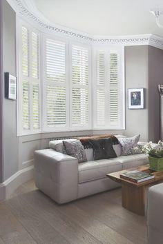 a living room filled with white furniture and windows covered in plantation shutters, next to a coffee table